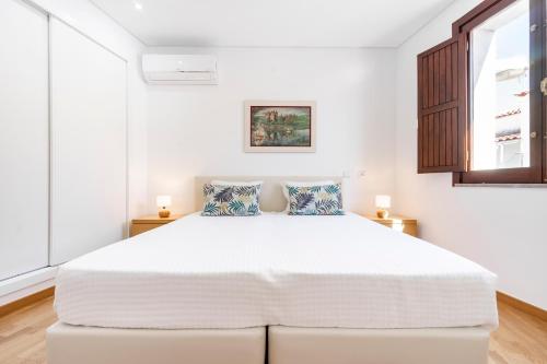 a white bedroom with a large bed with two pillows at Apartamento 1º de Maio in Tavira