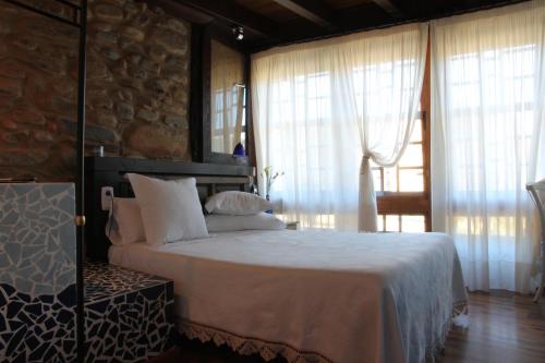 a bedroom with a bed with white sheets and windows at Micro-Hostal La Puerta del Perdón in Villafranca del Bierzo