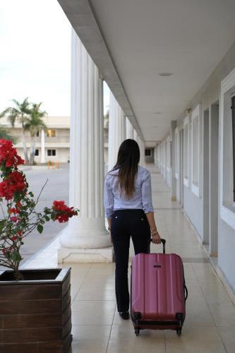 a woman walking down a hallway with a pink suitcase at Hotel Santorian in Hermosillo