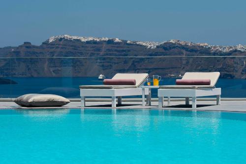 two chairs and a table next to a swimming pool at Acroterra Rosa Luxury Suites & Spa in Akrotiri
