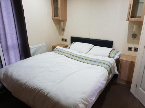 a bedroom with a large bed with white sheets at Park Home at Golden Sands Holiday Park in Foryd