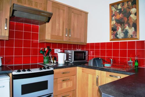 a red tiled kitchen with a stove and a microwave at 6 Northgate Vennel, Peebles in Peebles