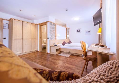 a bedroom with a bed and a desk and a television at Garni Lanzinger in Selva di Val Gardena