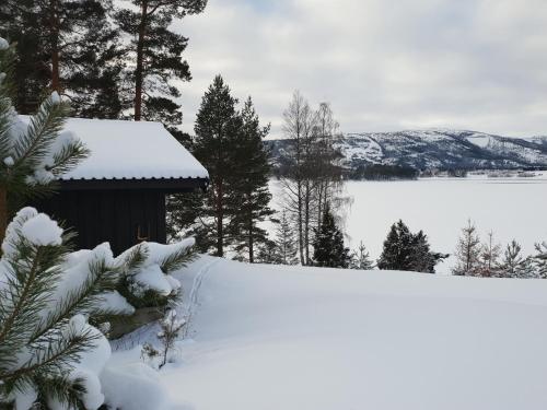 a snow covered yard with a shed and a body of water at Nedre Strand Hytteutleie in Vradal
