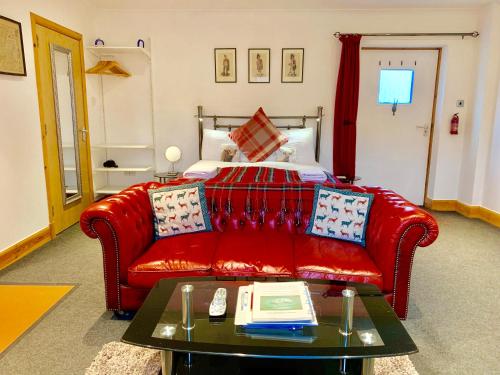 a living room with a red couch and a bed at Garrison Farm with Hot Tub in Inversnaid
