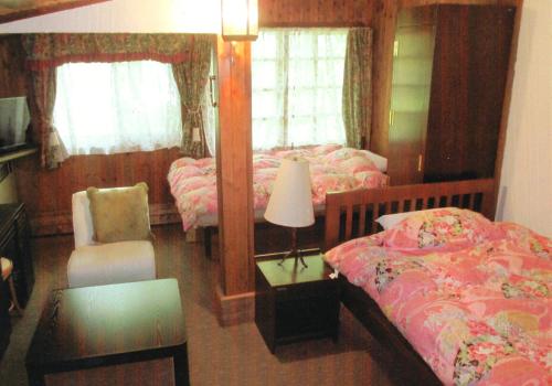 una camera con 2 letti, una lampada e una sedia di Pension Hakuba 70 a Hakuba
