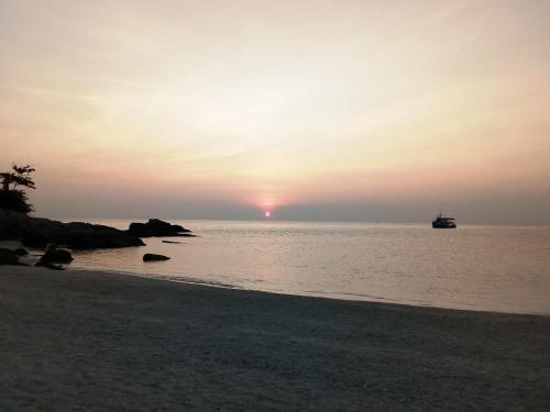 a sunset on the beach with a boat in the water at Nangyuan Island Dive Resort in Koh Tao