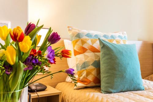 a bed with colorful pillows and a vase of flowers at Geneva Hotel in Sofia