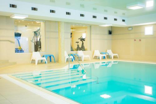 una piscina en una habitación con sillas blancas en Hotel Cieplice MEDI & SPA, en Jelenia Góra