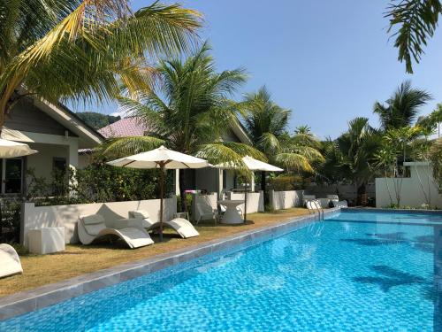 a pool with chairs and umbrellas next to a resort at Fuuka Villa in Pantai Cenang