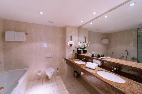 uma casa de banho com 2 lavatórios, uma banheira e um WC. em Atomis Hotel Munich Airport by Mercure em Oberding