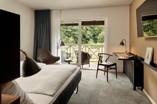 a bedroom with a bed and a desk and a balcony at Comwell Kongebrogaarden in Middelfart