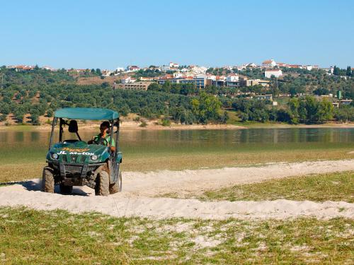 a green atv driving on a dirt road next to a river at AP Lago Montargil - Conference & SPA in Montargil