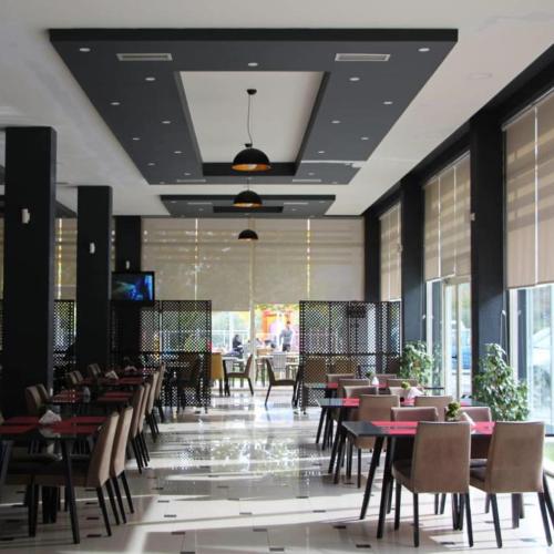 a dining room with tables and chairs and windows at Hotel Auto Grill Roberti in Tepelenë