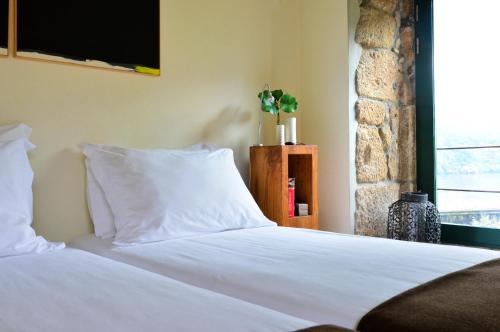 a bedroom with a bed with white sheets and a window at Casas de Pousadouro in Baião