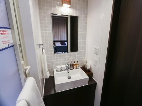 La salle de bains est pourvue d'un lavabo blanc et d'un miroir. dans l'établissement HOTEL LiVEMAX Sendai Aobadori, à Sendai