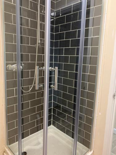 a shower with black tiles and a glass door at Cotswold Valley Aparthotel in Stroud