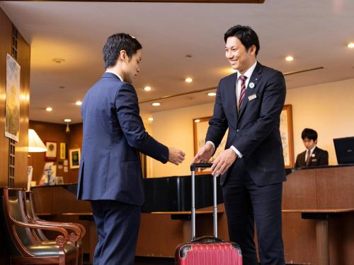 dos hombres de traje estrechando la mano con una maleta en Ark Hotel Kumamotojo Mae -ROUTE INN HOTELS-, en Kumamoto