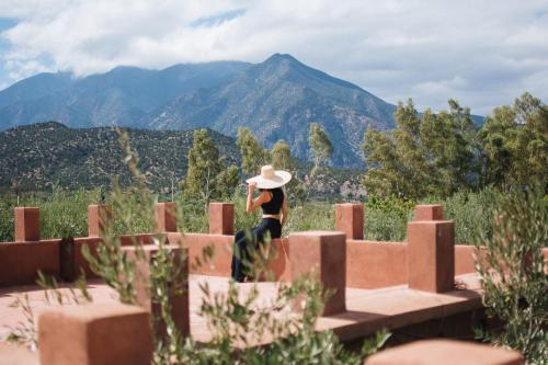 Une femme dans un chapeau assise sur un mur avec des montagnes dans l'établissement Ksar Shama, à Ouirgane