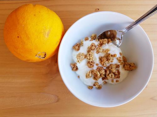 a bowl of cereal and an orange with a spoon at Casa dos Caldeiras in Lajes do Pico