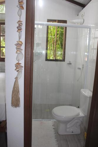 a bathroom with a toilet and a shower with a window at Chalé Paúba 80m do Mar in Pauba