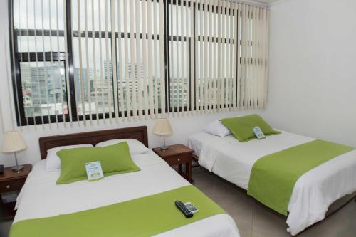 two beds with green and white sheets in a room with windows at Hotel Castell - Cerca Del Aeropuerto in Guayaquil