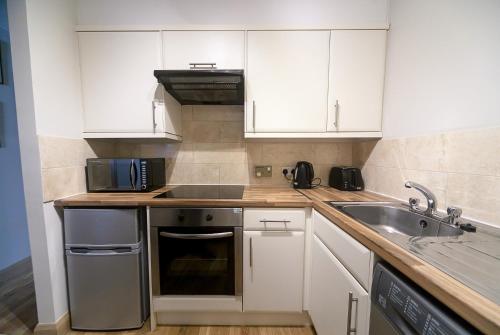 cocina con armarios blancos, fregadero y microondas en Ardconnel Apartment, en Inverness