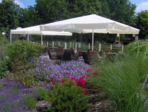 a garden with a white umbrella and chairs and flowers at Hotel Wikinger in Zempin