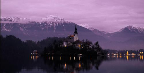 una chiesa su un'isola in acqua con montagne di Deluxe apartments Bled a Bled