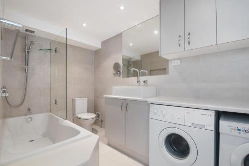 a white bathroom with a sink and a washing machine at Wharf Lodge River View Apartment in Maroochydore