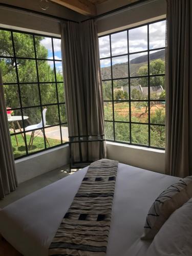a bedroom with a bed and large windows at De Kombuys in Oudtshoorn