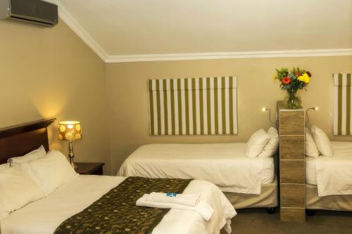 a hotel room with two beds and a vase of flowers at Mondior Manor Guest House in Kimberley