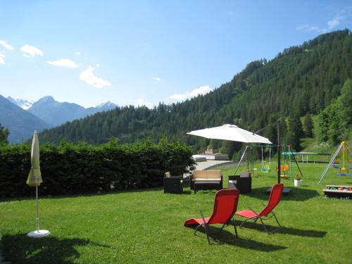 two chairs and an umbrella in a field with mountains at Lärchenhof Serfaus in Serfaus