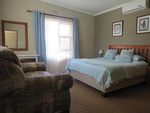 a bedroom with a bed and a chair and a window at Haus Victoria Self Catering Cottages in Oudtshoorn
