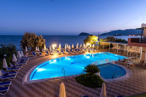a pool with chairs and umbrellas and the ocean at night at Mediterranean Beach Resort in Laganas