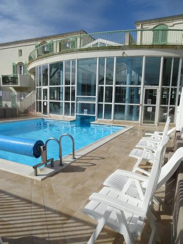 - une piscine avec des chaises blanches à côté d'un bâtiment dans l'établissement Ile de Ré - Proche plage - Hammam - Sauna - Piscine - 4 personnes, à Saint-Martin-de-Ré