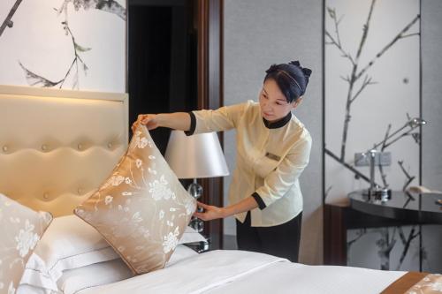a woman putting a pillow on a bed at Huaqiang Plaza Hotel Shenzhen, Enjoy Complimentary Mini Bar & Night Snack, Add breakfast - enjoy complimentary afternoon tea in Shenzhen