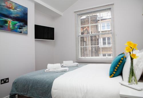 a white bedroom with a large bed and a window at Soho Suites by Indigo Flats in London