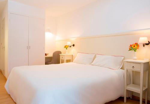 - une chambre blanche avec un grand lit blanc et 2 tables dans l'établissement Le Roussillon, à Amélie-les-Bains-Palalda