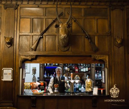 un hombre detrás de una barra con una cabeza de ciervo en la pared en Miskin Manor Hotel, en Hensol
