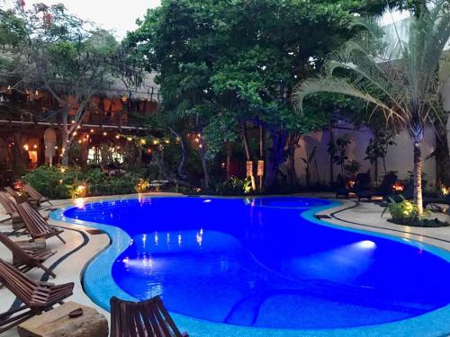 a large blue swimming pool with chairs and trees at Hotel El Pueblito in Holbox Island