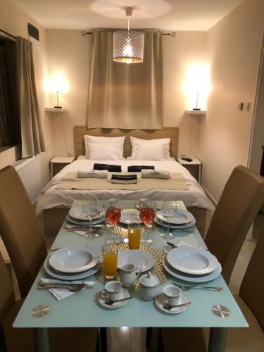 a table with plates and glasses on it with a bed at Mandula Apartman in Cegléd