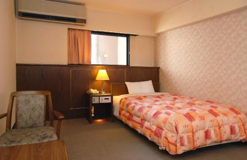 a hotel room with a bed and a chair and a window at Hotel New Plaza Kurume in Kurume