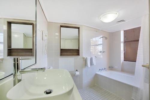 a white bathroom with a tub and a sink and a bath tubermott at Cosmopolitan apartment at College St in Sydney