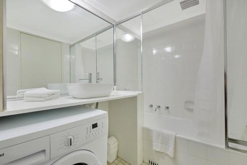 een witte badkamer met een wastafel en een wasmachine bij City apartment at College St in Sydney
