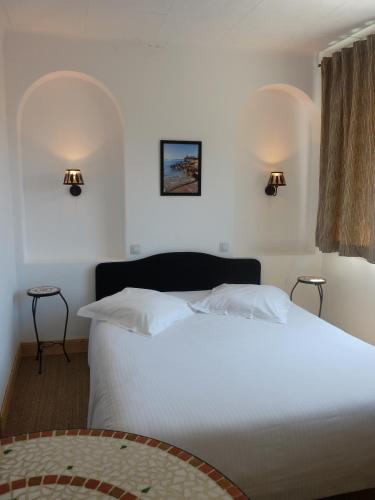 - une chambre avec un lit blanc et deux lumières sur le mur dans l'établissement Hôtel L'Oustaou, au Lavandou