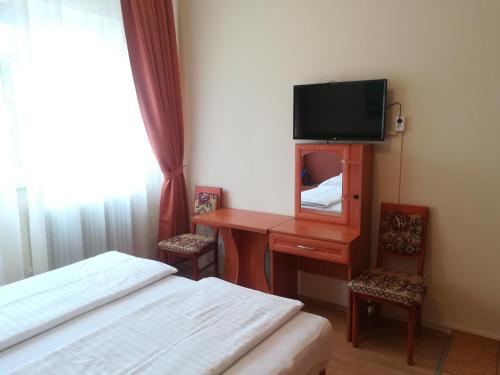1 dormitorio con 2 camas y escritorio con TV en Áldos Panzió en Farád