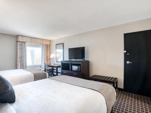 a hotel room with two beds and a flat screen tv at Alexis Hotel & Banquets Dallas Park Central Galleria in Dallas