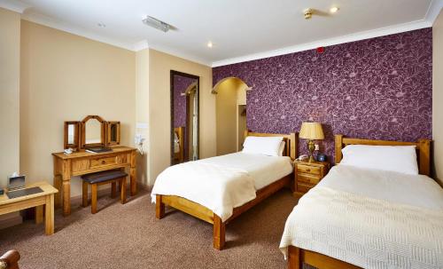 um quarto com 2 camas e uma parede roxa em The Feathers em Pocklington