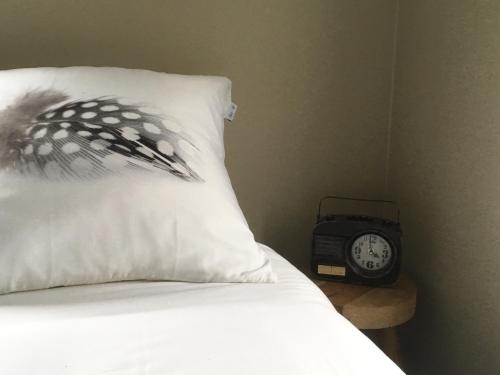 a bed with a pillow and an alarm clock on a table at Mooi, vrij gelegen vakantiehuis dichtbij zee en strand! in Aagtekerke